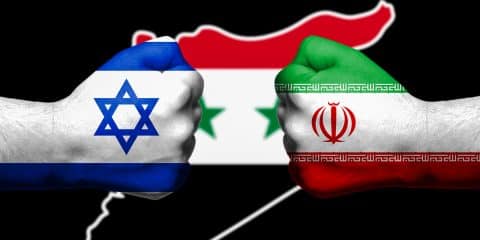 Flags of Israel and Iran painted on two clenched fists facing each other with flag of Syria in the background/Israel - Iran conflict concept