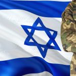 Crossed arms Israeli soldier with national waving flag on background - Israel Military theme.