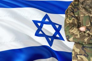 Crossed arms Israeli soldier with national waving flag on background - Israel Military theme.