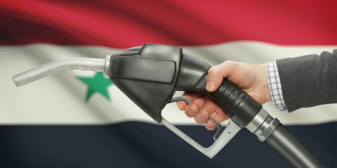 Fuel pump nozzle in hand with flag on background - Syria