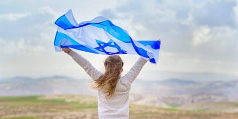 Little patriot jewish girl standing and enjoying with the flag of Israel on blue sky background.Memorial day-Yom Hazikaron, Patriotic holiday Independence day Israel - Yom Haatzmaut concept