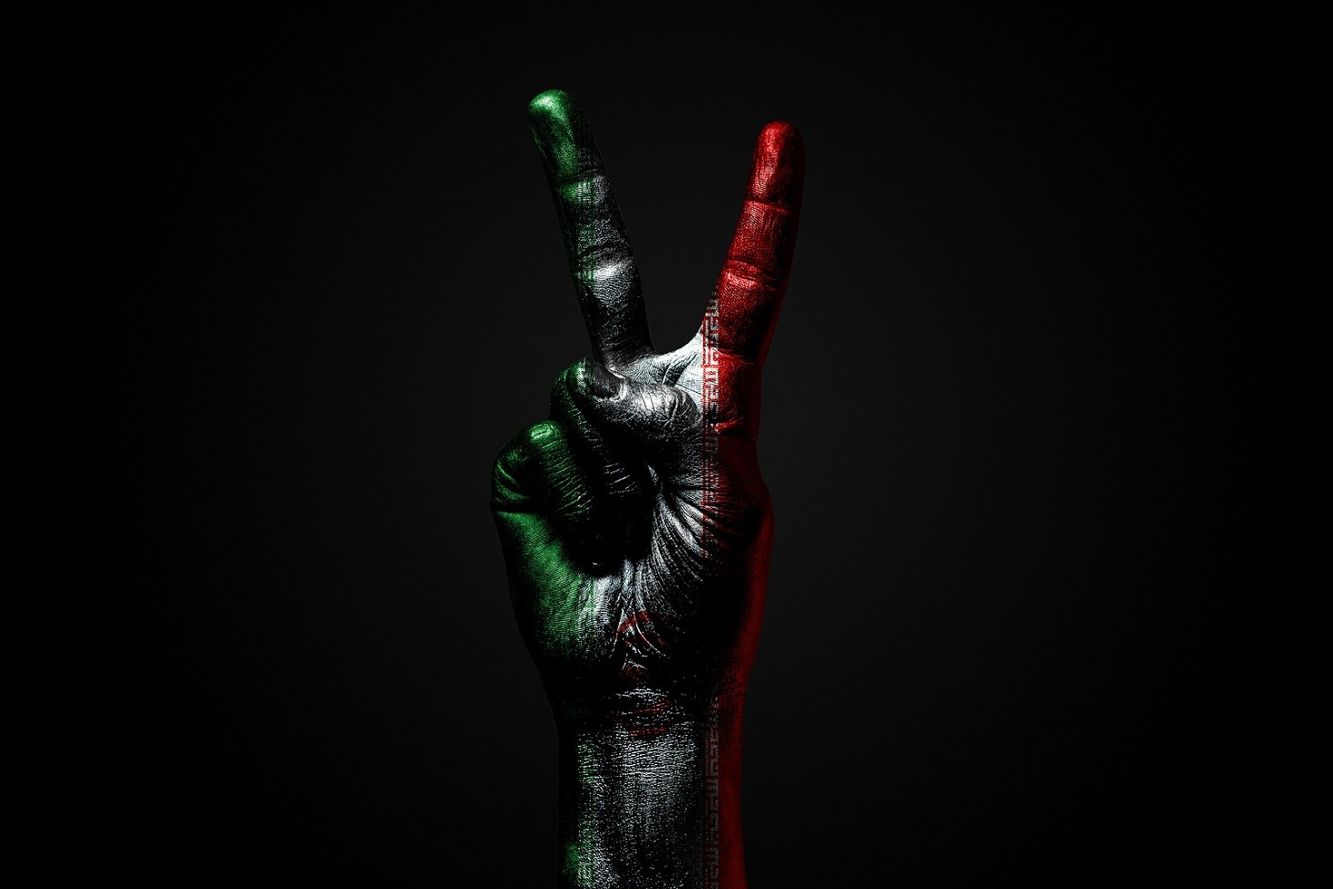 A hand with a painted Iran flag shows a fig, a sign of aggression, disagreement, a dispute on a dark background. Horizontal frame