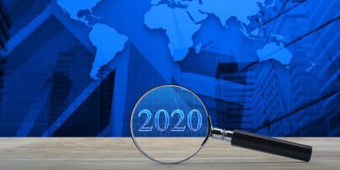 Magnifying Glass With 2020 Text And Financial Graph On Wooden Ta