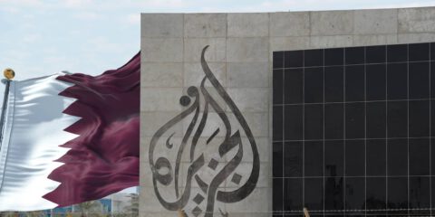 Al Jazeera building in Doha, with the flag of Qatar, illustration.