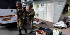 Israeli soldiers walk past the bodies of people, some of them elderly, that lie on a street after they were killed during a mass-infiltration by Hamas gunmen from the Gaza Strip, in Sderot